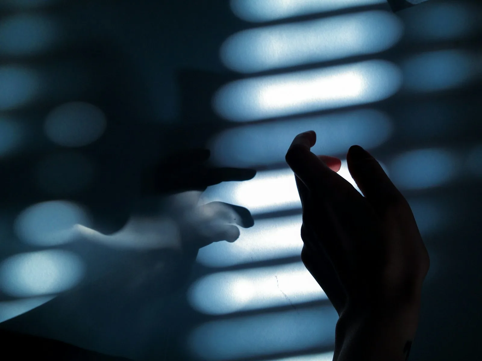 A hand reaching toward strips of light, with a faint ghosted second hand beside it