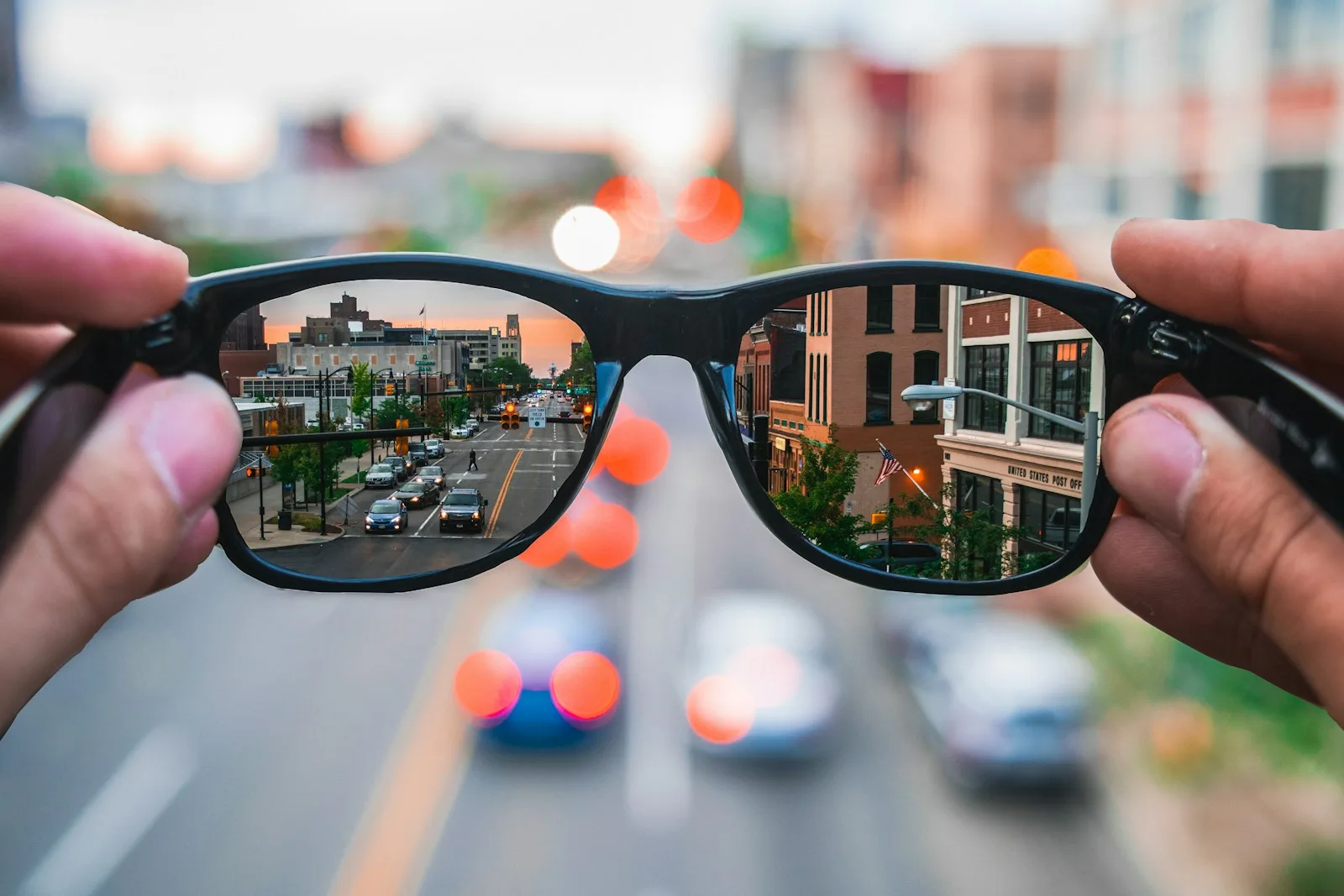 A pair of glasses held up to a city street, the scene appearing sharper through the lenses
